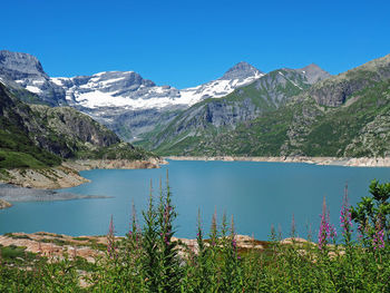 Scenic view of lake by mountains against clear blue sky