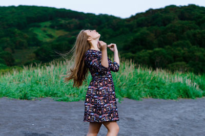 Young woman standing on grass against sky