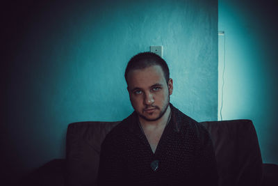 Portrait of young man sitting against wall