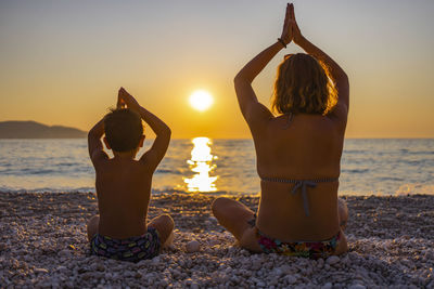 Rear view of women sitting at beach during sunset