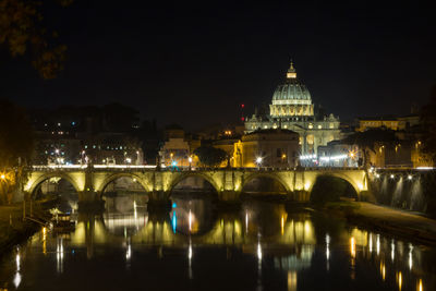 Illuminated bridge over river against buildings at night