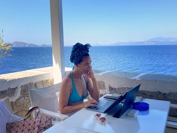 Mature woman using laptop at tourist resort against sea