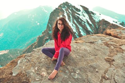 Full length portrait of young woman sitting on mountain