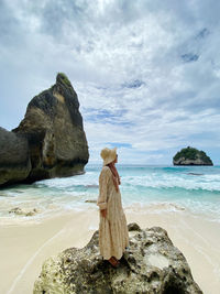 Rear view of woman standing at beach against sky