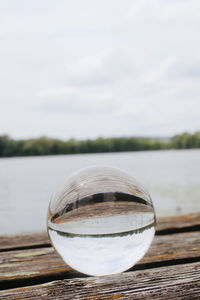 Close-up of glass ball on table against lake