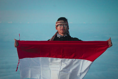 Portrait of man holding red boat in sea against sky