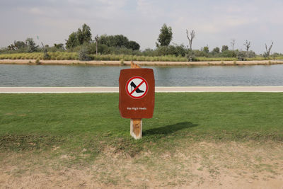 Information sign on field by lake against sky