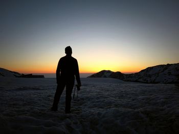 Rear view of silhouette photographer standing on snow covered field against clear sky during sunset