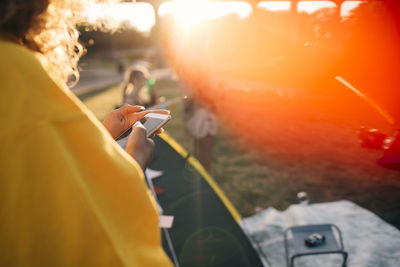 Cropped image of woman using mobile phone while standing by tent on sunny day