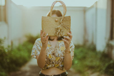 Woman holding wicker bag while standing outdoors