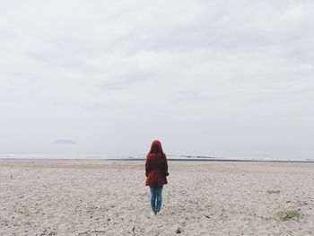 Rear view of woman standing at beach against sky