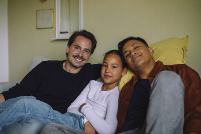 Portrait of smiling gay couple sitting with daughter on sofa at home