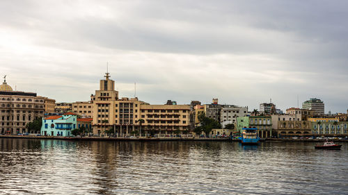 View of buildings by river against cloudy sky