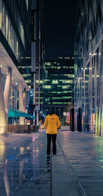 Rear view of man walking on wet street at night