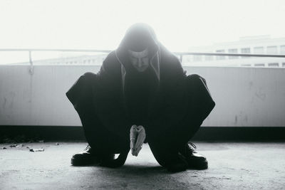 Full length of man wearing costume crouching against retaining wall