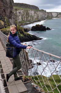 Full length of woman standing on rope bridge over sea against mountain