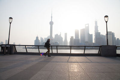 Side view of woman on sidewalk against city skyline