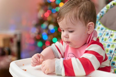 Little boy toddler eating in his high chair in front of the christmas tree