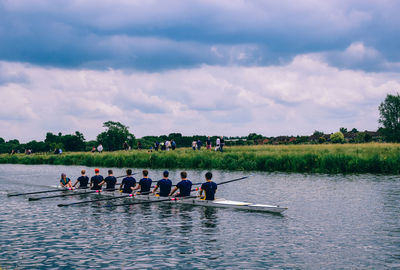 Men rowing on boat in river against cloudy sky