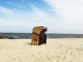 Hooded beach chair on sand against sky