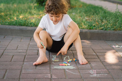 Little preschool boy draws with colorful chalks on the ground.