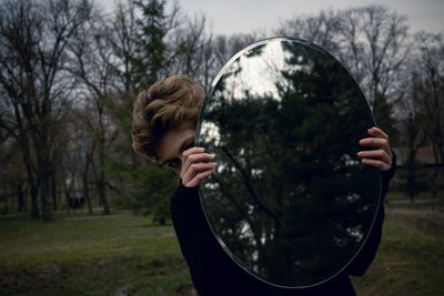 Close-up of young woman holding mirror with reflection at park