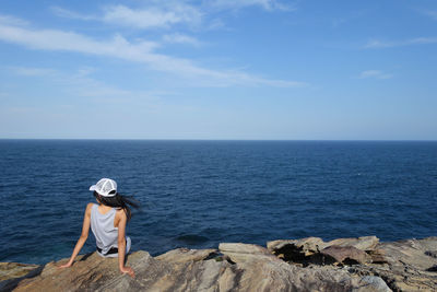 Rear view of mature woman sitting by sea against sky