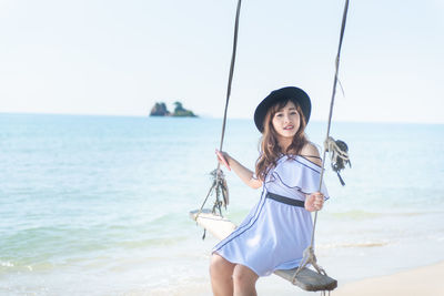 Portrait of young woman holding sunglasses at beach against sky