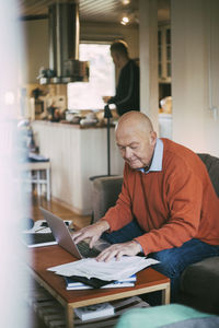 Elderly gay man using laptop while calculating financial bill at home