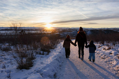 Rear view of people walking on snow covered field against sky during sunset