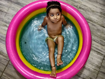 High angle view of cute girl sitting in wading pool at home