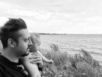 Man with baby girl looking at sea against sky