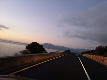 Road by trees against sky during sunset