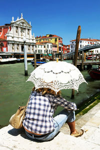 Woman carrying white umbrella looking at santa maria di nazareth while resting by grand canal