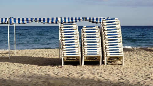 Hooded chairs on beach against sky