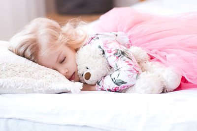 Girl sleeping with teddy bear on bed at home