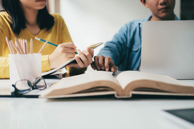 Midsection of friends reading book while sitting at table