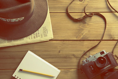 High angle view of vintage camera by spiral notepad by hat on newspaper over table