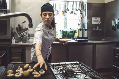 Female chef arranging mushrooms on barbecue grill in commercial kitchen