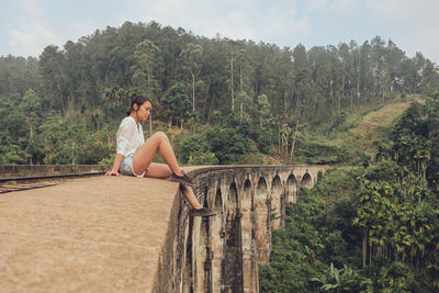 Woman sitting on bridge against mountains