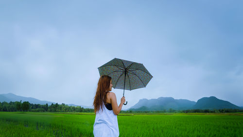 Rear view of woman with umbrella on field against sky