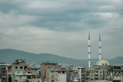 Buildings and mosqu in city against cloudy sky