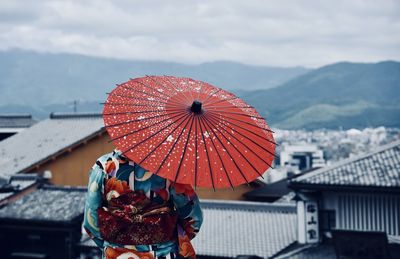 Rear view of woman under umbrella standing by house roofs in city