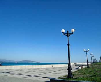 Street light by sea against clear blue sky