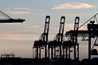 Silhouette cranes at pier against sky during sunset