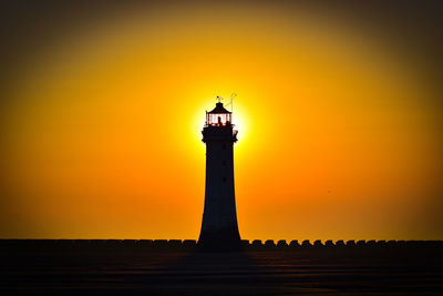 Silhouette lighthouse by sea against orange sky