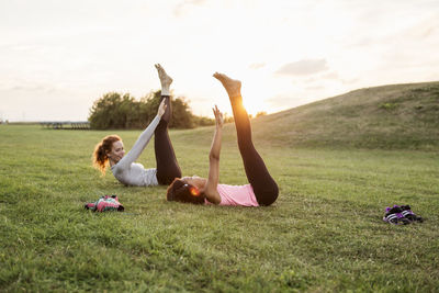 Side view of woman looking at daughter exercising on grass at park during sunset