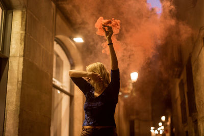 Woman standing by illuminated lamp at night