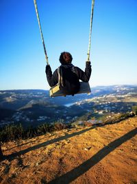 Rear view of woman swinging on field against sky