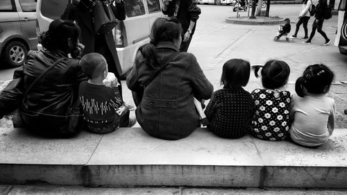 Rear view of women and children sitting on retaining wall